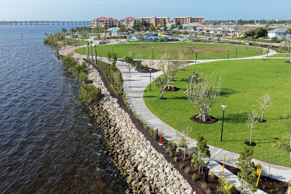 Waterfront boardwalk at Jaycee Park with railings and benches curves above a rocky shoreline next to green lawns.